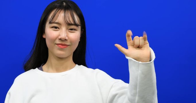 Asian beautiful girl making sign language "i love you" with fingers on blue screen