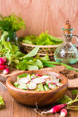 Lenten spring vegetable salad of cucumber, radish, greens and sunflower oil in a plate on a wooden table