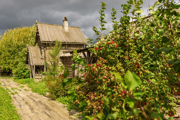 An old wooden house and a path to it in the summer in cloudy weather.
