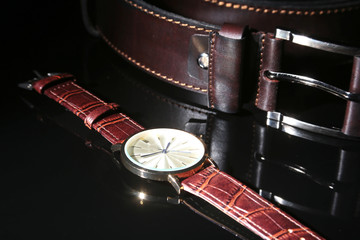 Men's accessories with brown leather wallet, belt and watch on black mirror background