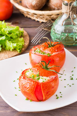 Fresh tomatoes baked with cheese and egg sprinkled with green onions on a plate on a wooden table