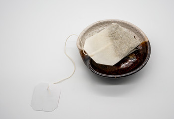 Teabag with white tag on brown ceramic plate on white background