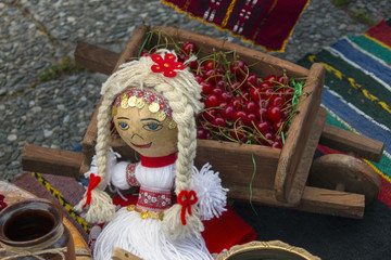 Doll in a typical Bulgarian folk costume to a decorative cart with cherry.Kustendil, Bulgaria.