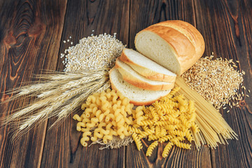 Foods high in carbohydrate on wooden background. Loaf, pasta, pearl barley and oats. - obrazy, fototapety, plakaty