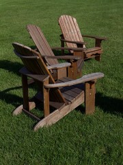 Close up view of rustic wooden Adirondack chairs with green grassy background
