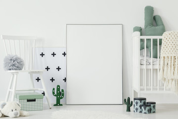 Grey pompom placed on white chair standing in bright baby bedroom interior with cactus shaped decor...