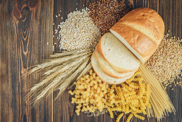 Foods high in carbohydrate on wooden background. Loaf, pasta, pearl barley and oats.