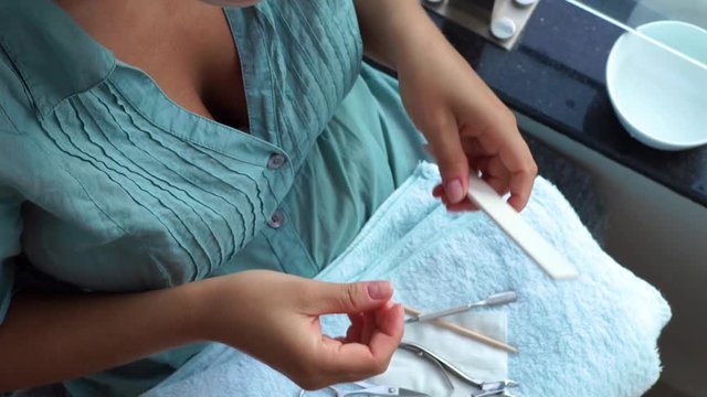Woman using manicure scissors for cut cuticle and filing nail with nail file while home manicure. Close up. Home manicure and nail care concept.
