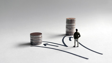 A miniature man standing in front of two paths with a stack of coins of different heights.