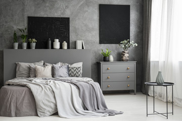 Moon canvas on a grey wall in a monochromatic cozy bedroom interior with a bed with cushions,...
