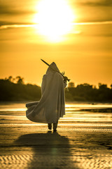 Portrait of assassin in white costume with the sword at the sea. He is posing at the sea during beautiful sunset. Yellow, soft light. - 212038738