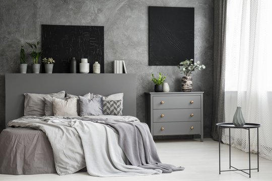 Moon canvas on a grey wall in a monochromatic cozy bedroom interior with a bed with cushions, bedding an a blanket. Real photo