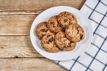 oatmeal cookies with chocolate slices in white plate and napkin on a wooden background