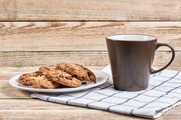 oatmeal cookies with chocolate slices in white plate and brown cup on napkin on a wooden background