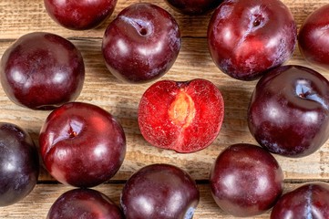 opened plum with a ossicle beside several plums on wooden background, close-up