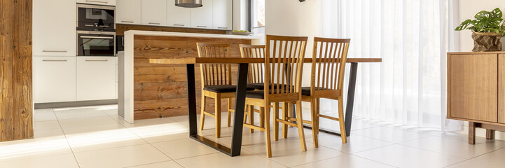 Real photo of wooden dining table with four chairs standing in open space kitchen interior with...