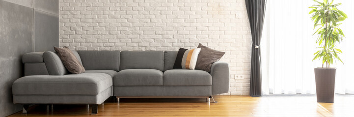 Grey corner sofa with decorative cushions in the real photo of bright living room interior with...