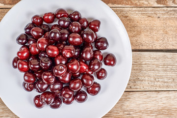 cherry in a white plate on a wooden background, flat lay