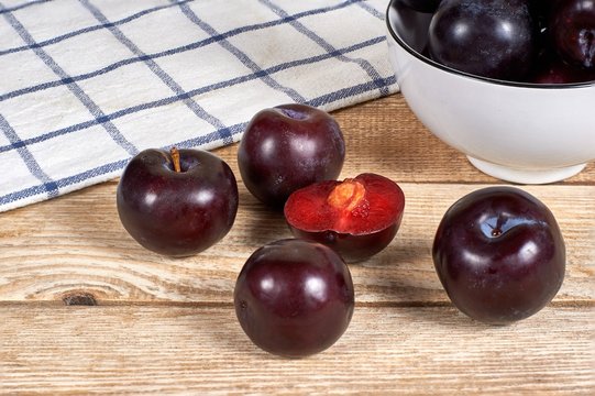 opened plum with a ossicle beside several plums, in front of bowl with red plums and on wooden background