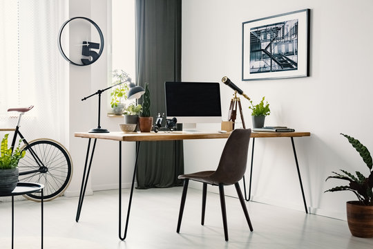 Hairpin desk with mockup monitor, plants and telescope standing in bright room interior with poster on the wall and window with drapes