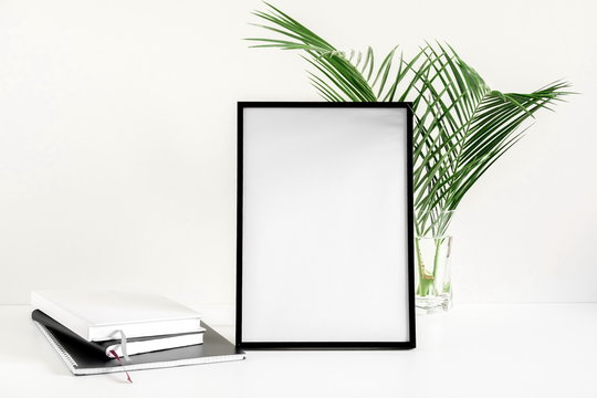 Front view blank mock up of photo frame on white background, notebook, green plant. Flat lay, top view, copy space 