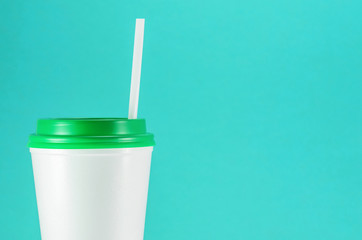 white plastic coffee cup with green lid on a blue background, front view with copy space