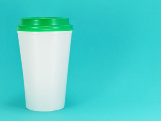 white plastic coffee cup with green lid on a blue background, front view with copy space