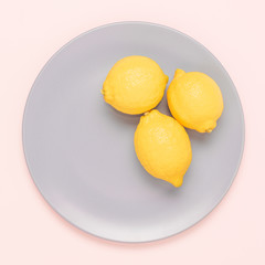 Three yellow lemons in the plate on pink background.