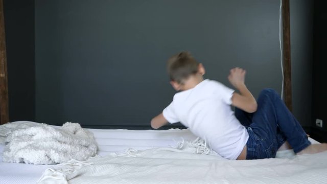 happy carefree boy doing somersaults on bed in slow motion at home