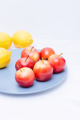 Fresh apples and lemons in a plate on white background.
