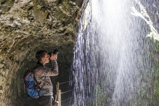 Young man taking photograph behind waterfall, Partnach Gorge, Upper Bavaria, Bavaria, Germany, Europe