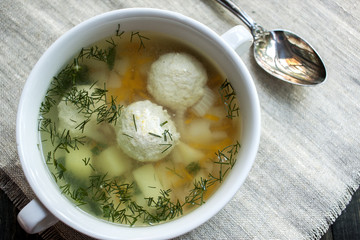 Soup with meatballs in a white bowl on the wooden background.