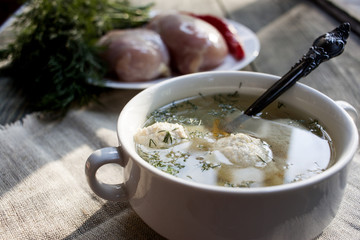 Soup with meatballs in a white bowl on the wooden background.