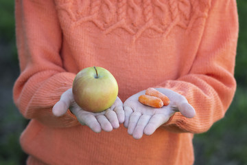 Baby hands close-up. A girl in an orange sweater is holding an apple and a small carrot