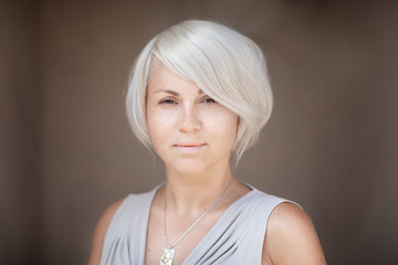 Stately serious blond woman looking solemnly directly in the camera. Blurred brown background.
