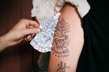 cropped shot of tattoo artist transferring tattoo sketch on shoulder in tattoo salon