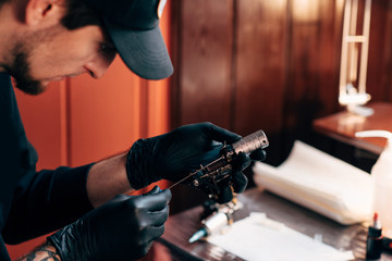 selective focus of tattoo artist in gloves with tattooing machine in salon