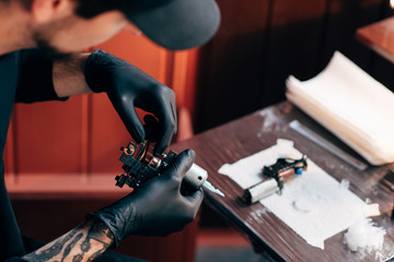 selective focus of tattoo artist in gloves with tattooing machine in salon