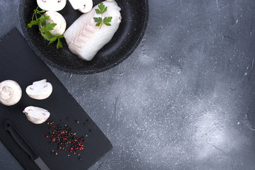 Preparation of a seafood dinner. Fillet of white fish on a black board with mushrooms and spices. Copy space.