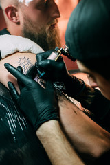 selective focus of tattoo artist in gloves with tattoo machine working on tattoo on shoulder in...