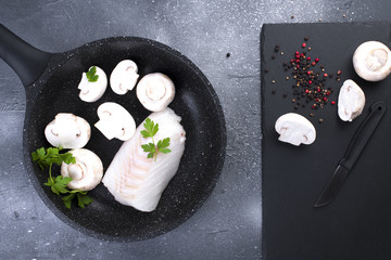 Preparation of a seafood dinner. Fillet of white fish in a black frying pan with mushrooms and spices. Copy space.