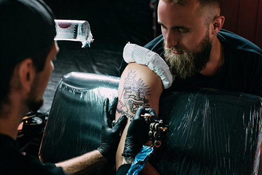 selective focus of tattoo artist in gloves with tattoo machine working on tattoo on shoulder in salon