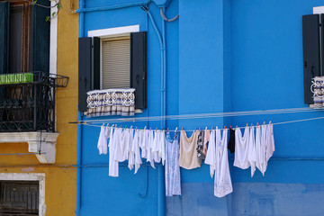 CLOSE UP: White towels dry in front of the vivid blue house in historic Venice.