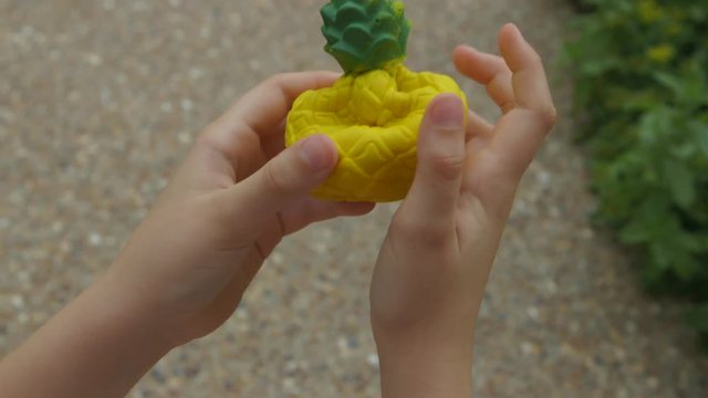 closeup POV of a pineapple squishy being squeezed by a little girl.