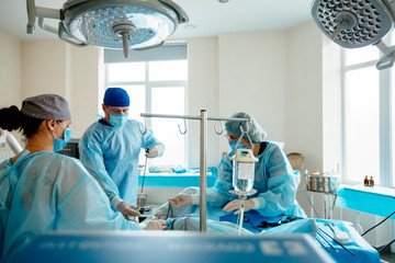 Surgeons team preforming operation in hospital operating theater, male surgeon operating...