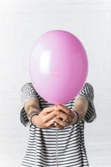 Girl holding pink balloon in front of her face on white brick wall background