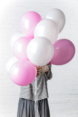 Woman holding pink and white balloons in front of her face on white brick wall background