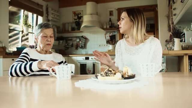 Elderly grandmother with an adult granddaughter eating biscuits at home.