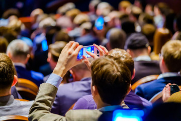 Man takes a picture of the presentation at the conference hall using smartphone