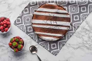 top view of delicious brown cake with sugar powder and fresh berries on marble surface